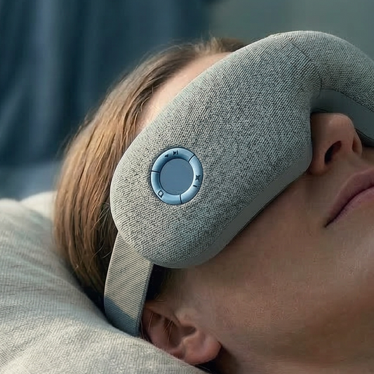 Person lying in bed wearing a gray sleep mask in a bedroom setting.